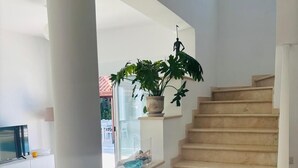 Una escala amb graons beix, un pilaret blanc i una planta en test.