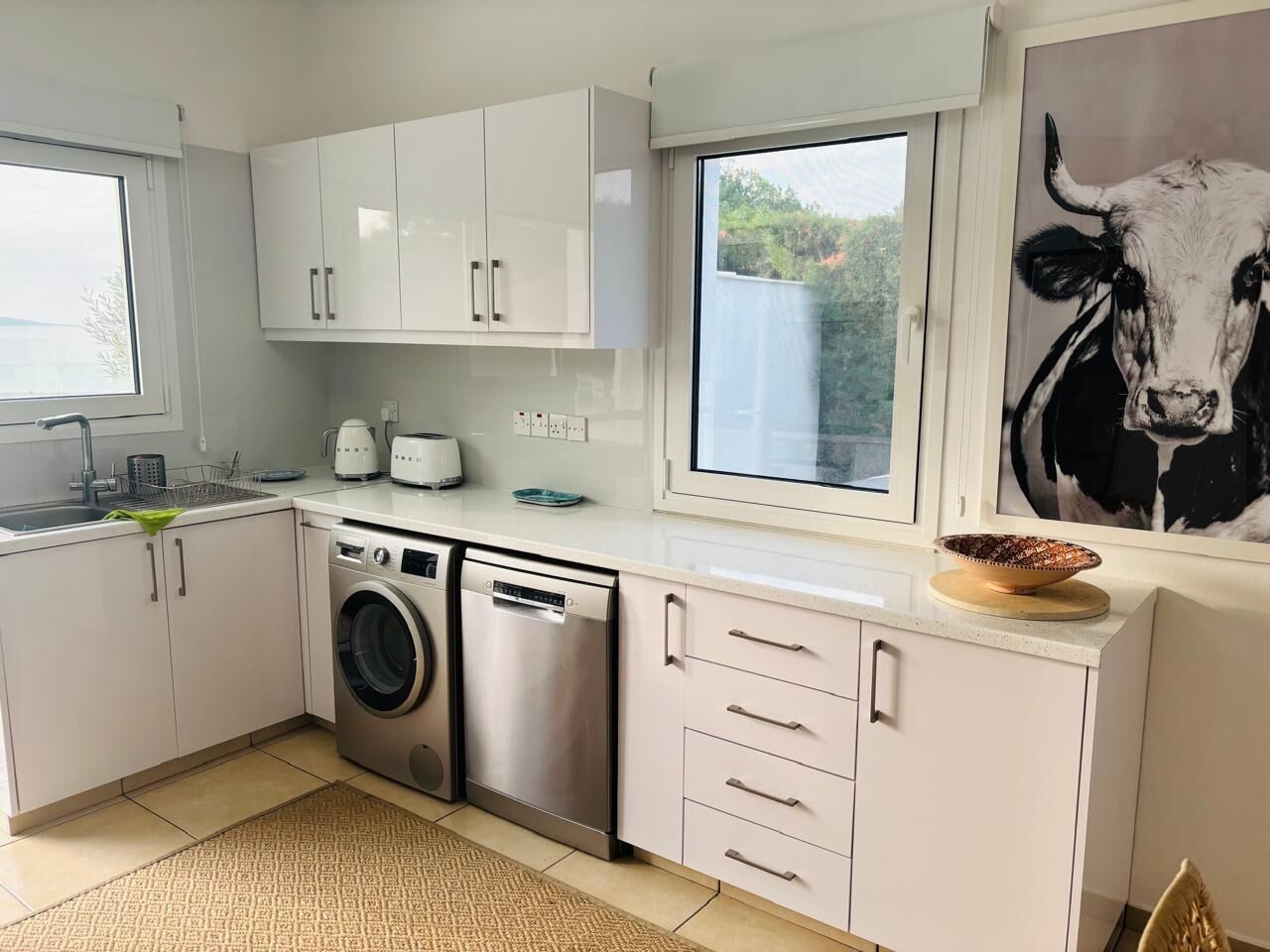 Une cuisine moderne avec des meubles blancs, un lave-linge et une grande fenêtre.