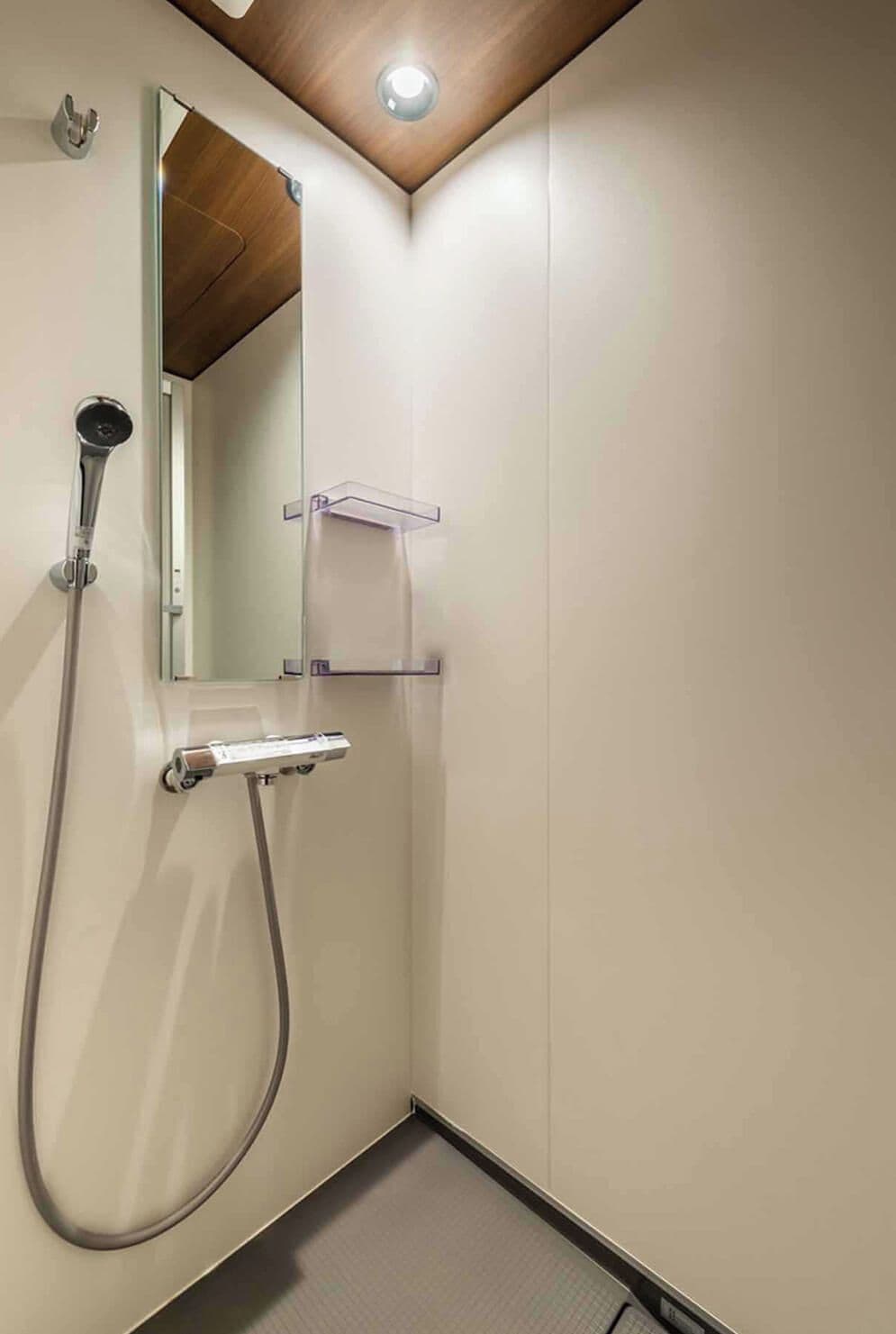 A modern bathroom with a shower, a mirror, and a wooden ceiling.