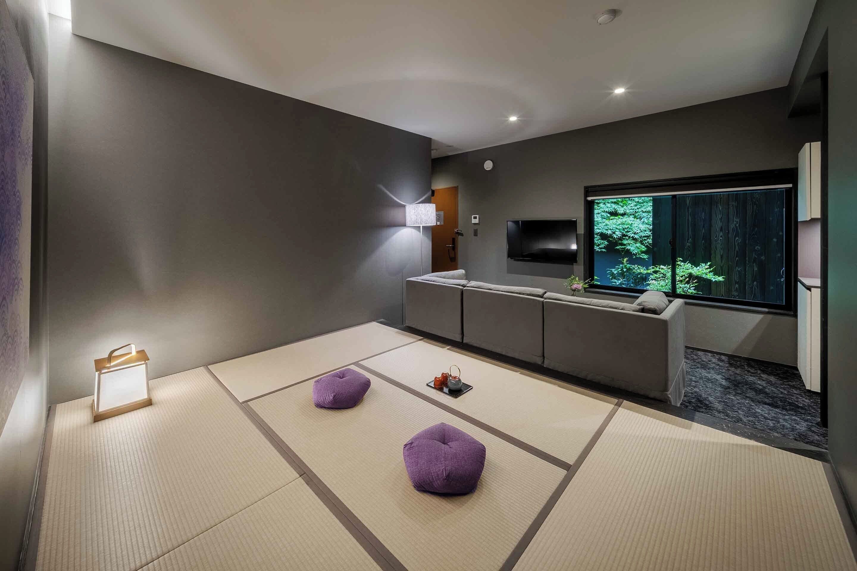 Une chambre moderne avec un sol recouvert de tatamis, un canapé, un téléviseur à écran plat et une grande fenêtre donnant sur un paysage verdoyant.