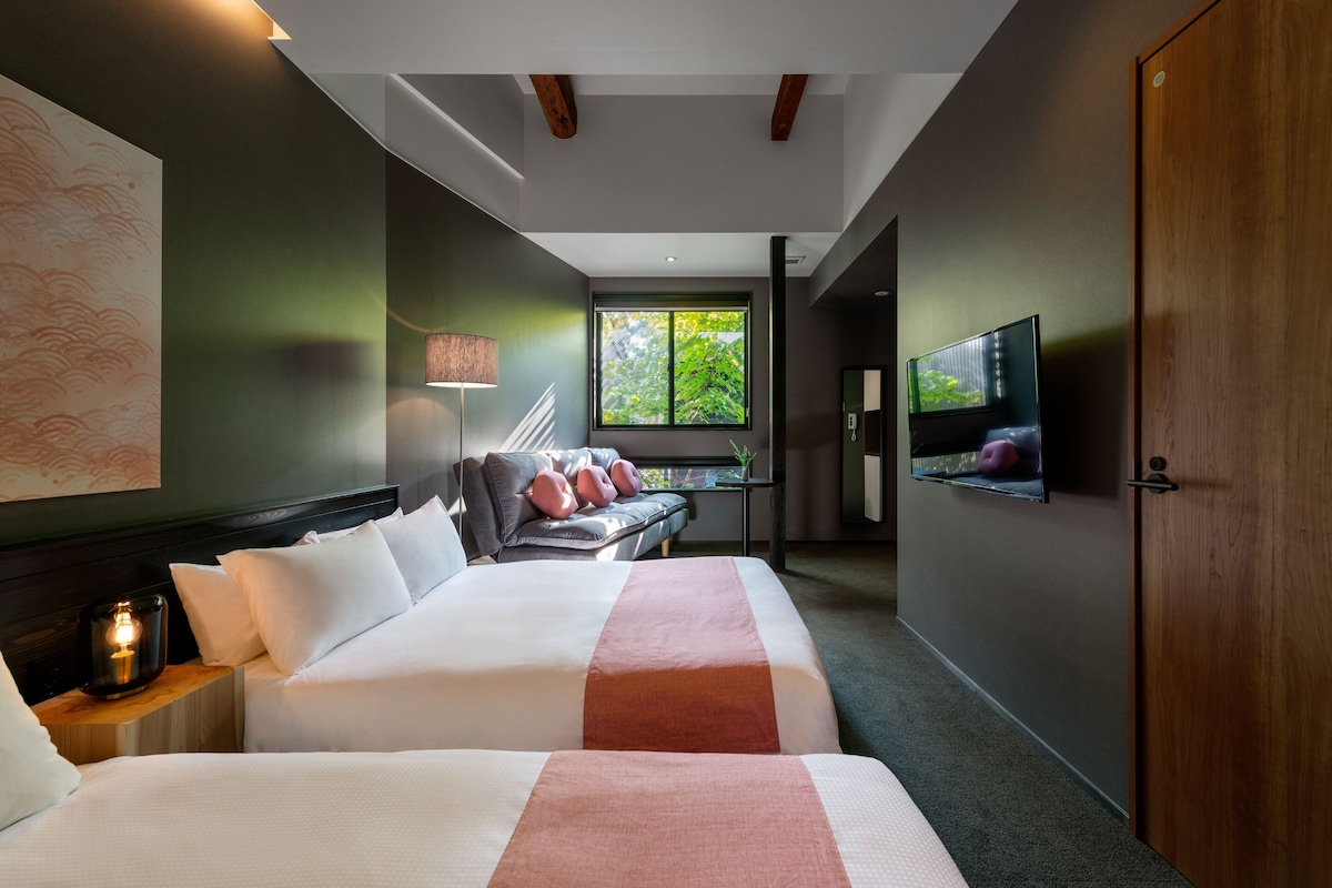 Et moderne hotelværelse med to senge, et stort vindue, et fjernsyn og et skrivebord med en plante.