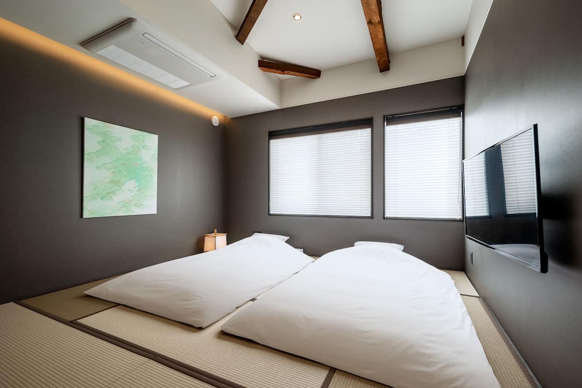 Een moderne slaapkamer met een groot bed, twee ramen, een flatscreen televisie en een kunstwerk aan de muur.
