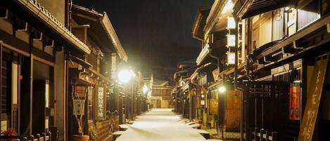 A narrow street lined with traditional buildings at night, illuminated by street lamps.