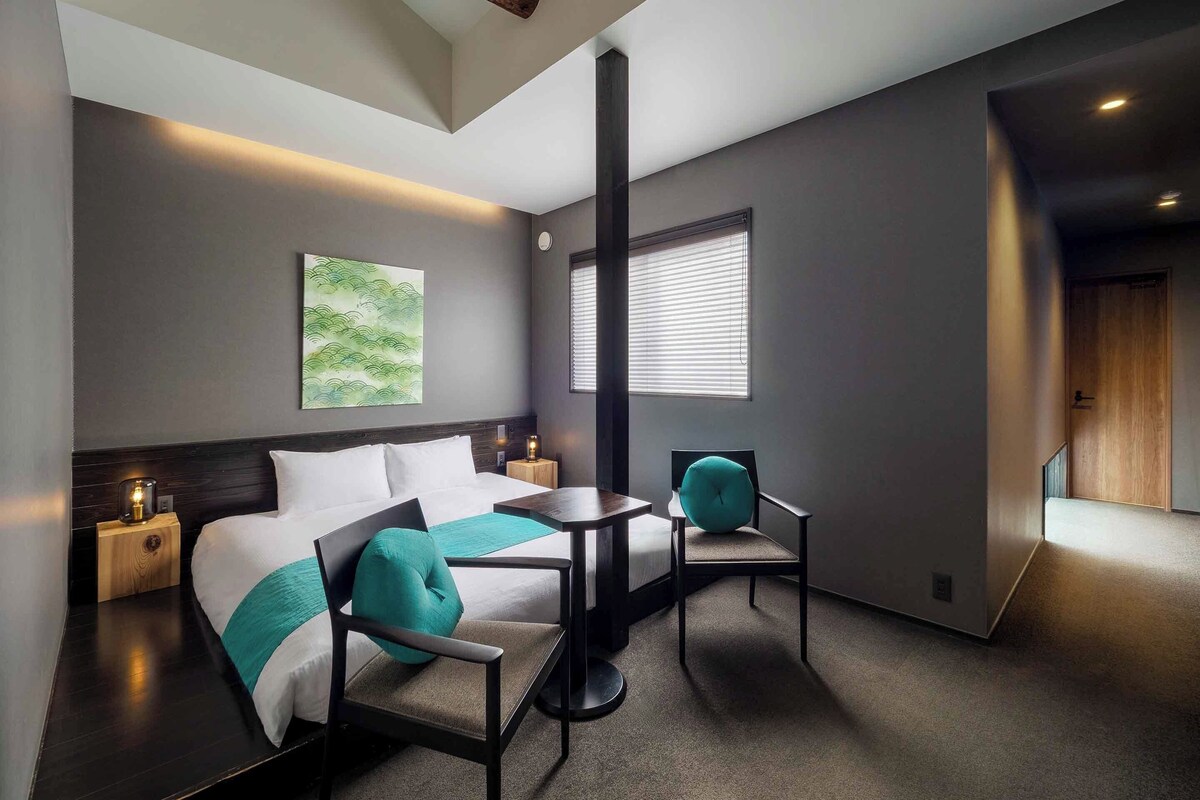 A modern hotel room with a bed, a desk, a chair, and a window with blinds.