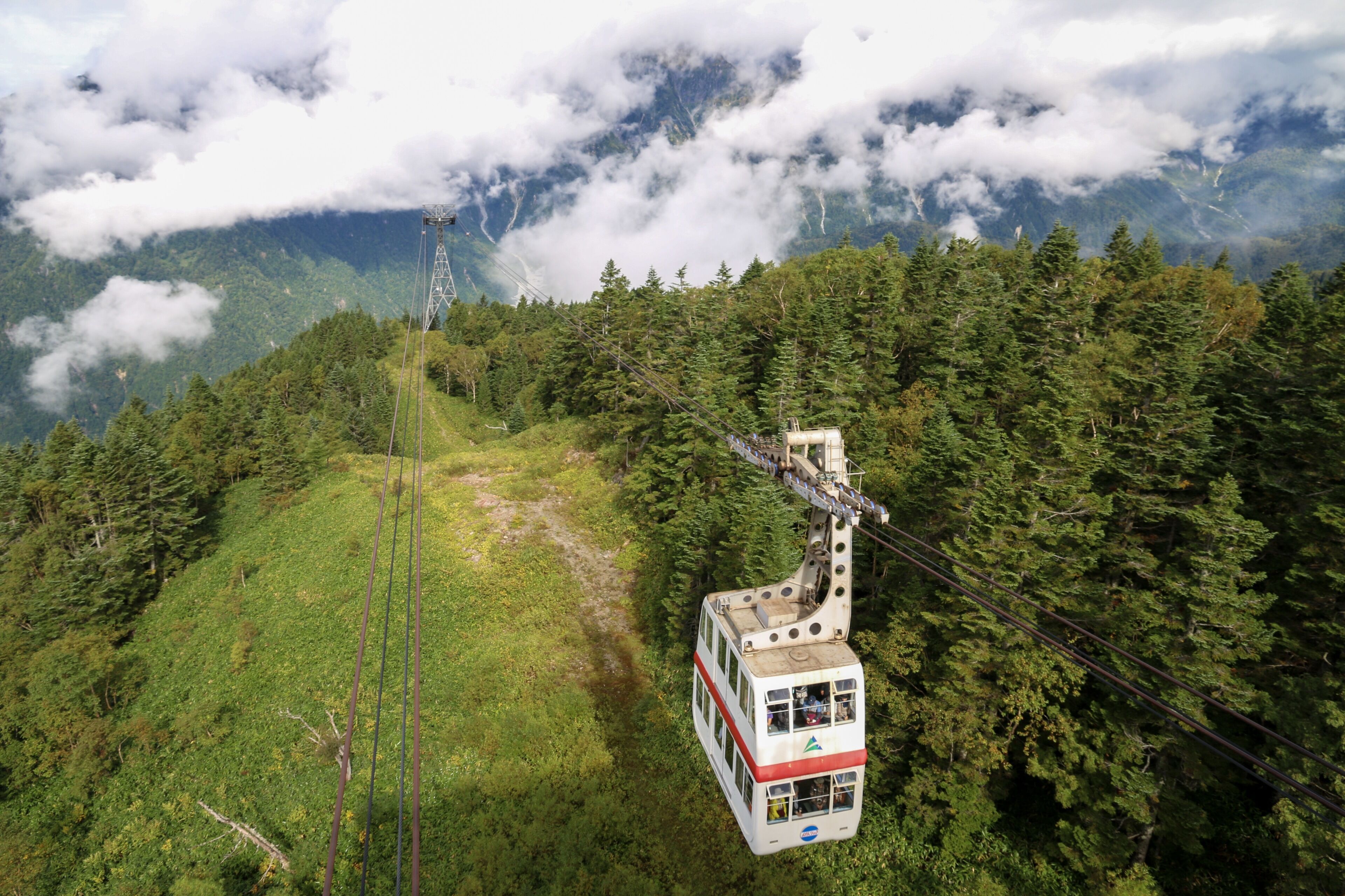 Um sistema de teleférico em área montanhosa com floresta densa e nuvens.