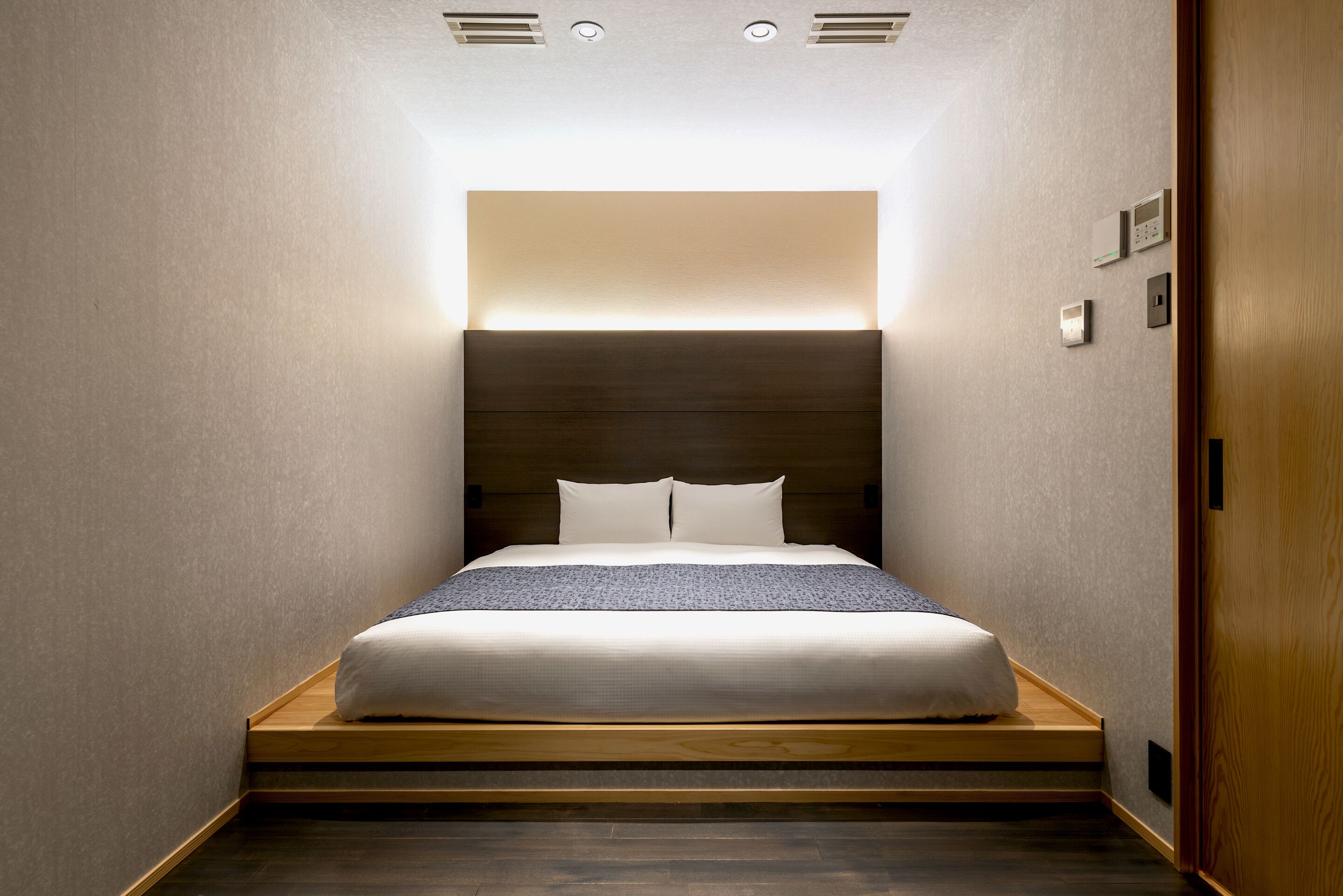 A modern bedroom with a built-in bed, recessed ceiling lighting, and a wooden platform.