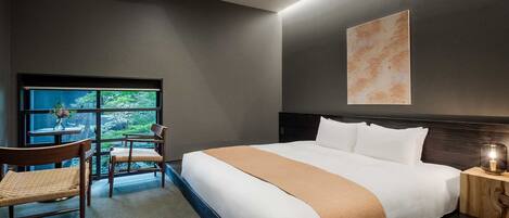 A hotel room with a large bed, a desk with a chair, a window with a view, and a wall-mounted artwork.