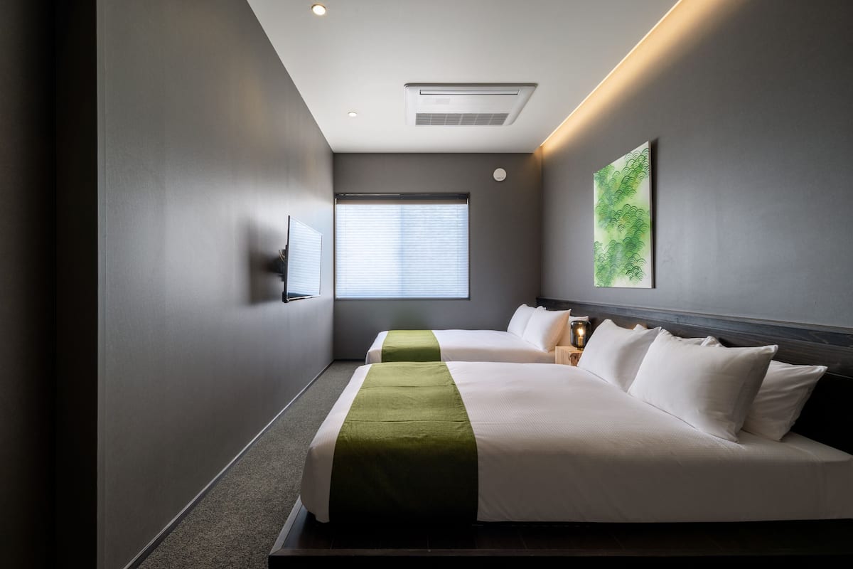 Een hotelkamer met twee bedden, een groot raam, een tv aan de muur en een schilderij.