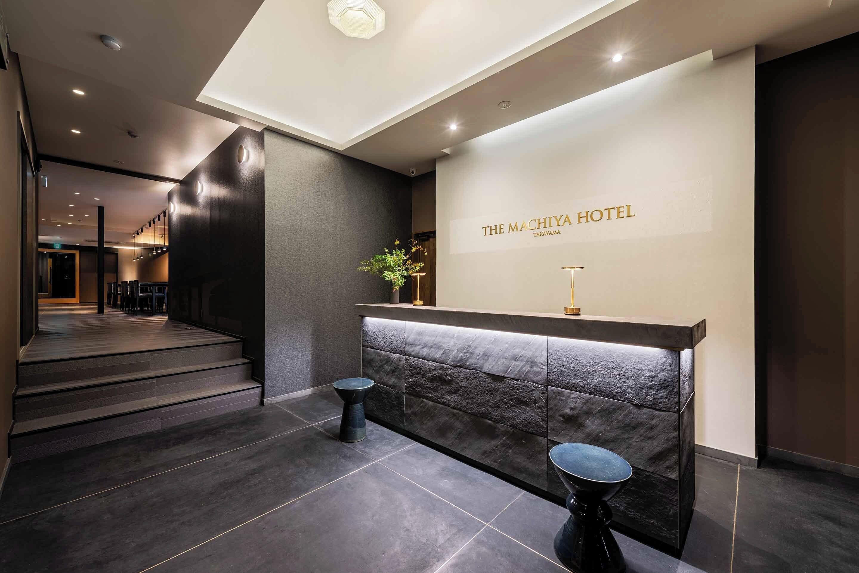A hotel reception area with a modern design, featuring a reception desk, a staircase, and a wall-mounted sign.