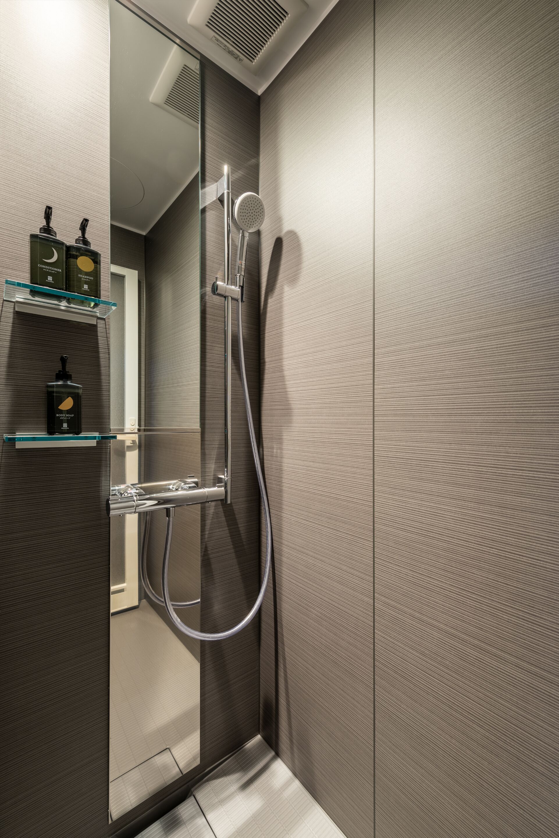 Ein modernes Badezimmer mit einer integrierten Dusche, einer Glasablage für Toilettenartikel und einer Spiegelwand.