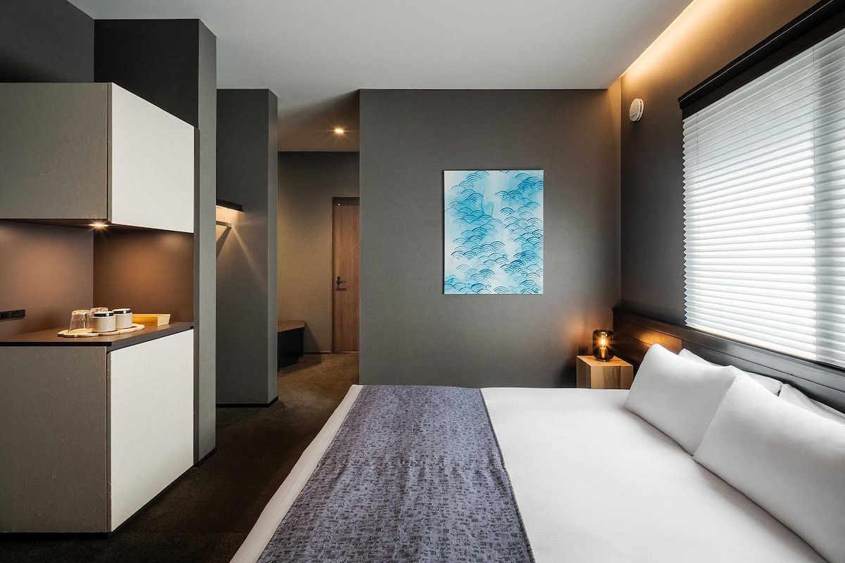 A modern hotel room with a bed, a desk, and a painting on the wall.