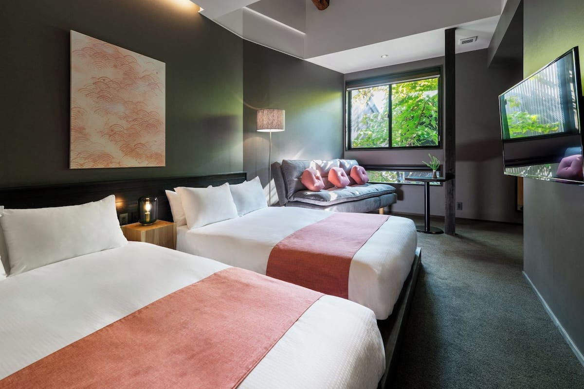 Een hotelkamer met twee bedden, een bureau, een televisie en een groot raam met uitzicht op groen.