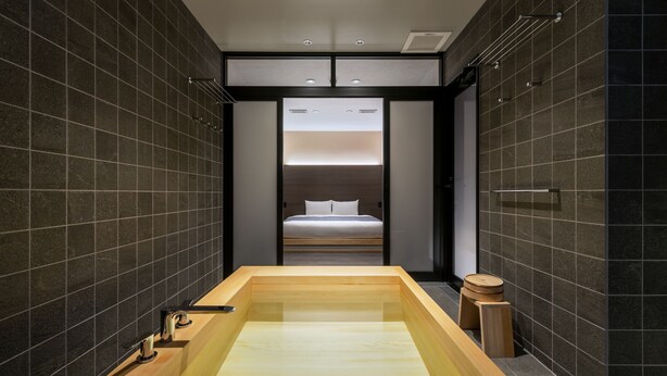 Een moderne badkamer met een groot bad, donkere betegelde wanden en een bed op de achtergrond.