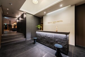 Un área de recepción de diseño moderno, con mostrador de recepción, una escalera y un letrero en la pared que dice "THE MACHIYA HOTEL".