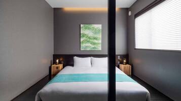 Quarto de hotel moderno com uma cama grande, duas mesas de cabeceira com luminárias, uma obra de arte na parede e uma janela com persianas.