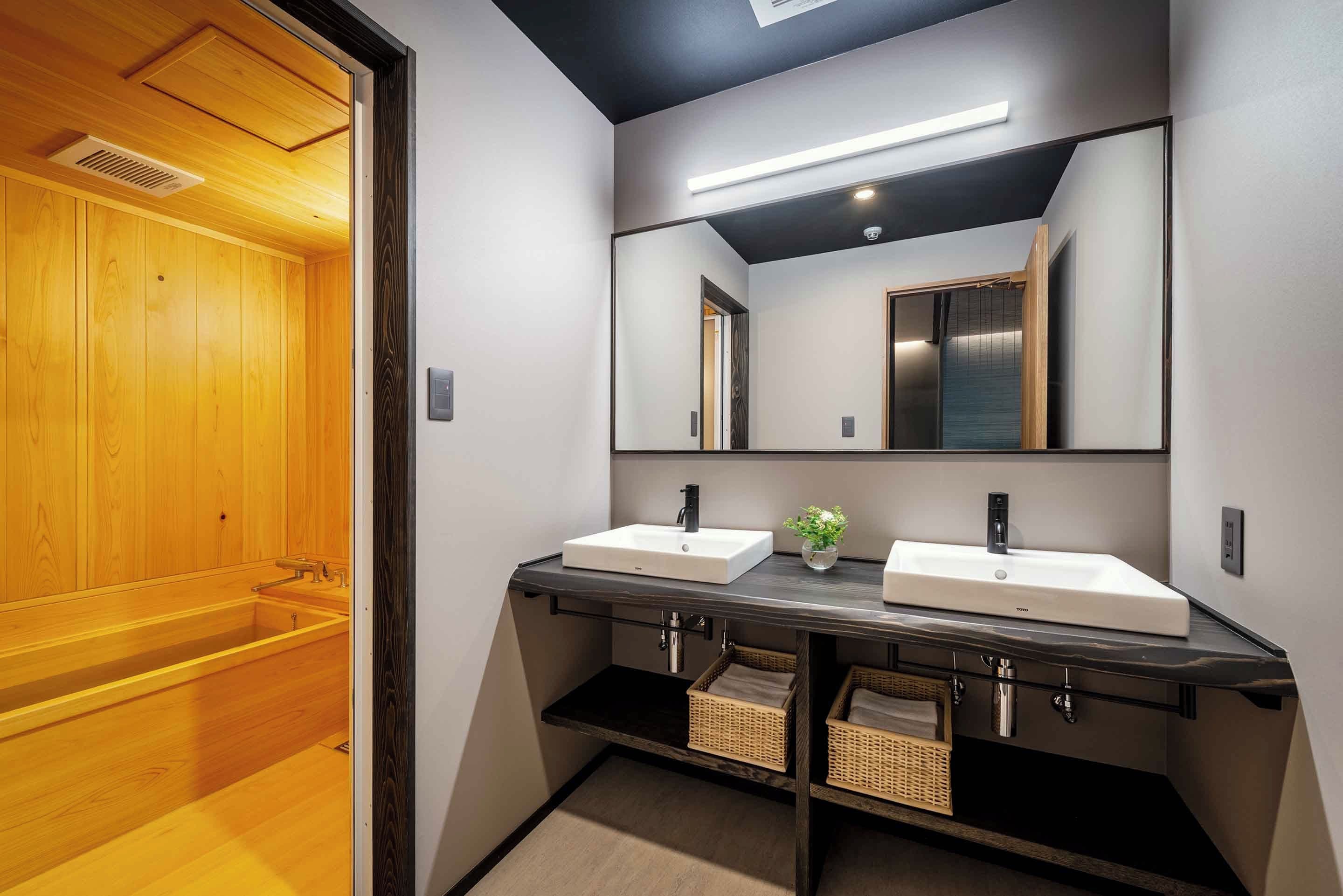 Une salle de bain moderne avec deux lavabos, un miroir et une porte de sauna en bois.