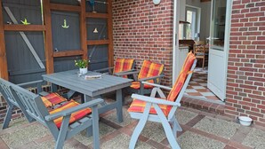 Un patio con tavolo e sedie, un muro in mattoni e una porta che dà su un ambiente interno.