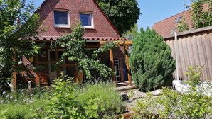 Una casa in mattoni con tetto a punta, un'uscita su un ponte di legno e un giardino con diverse piante e fiori.