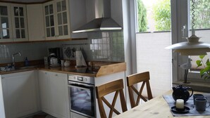 Cucina con mobili bianchi, un piano di lavoro in legno, forno, lavello e finestra con vista sul verde.