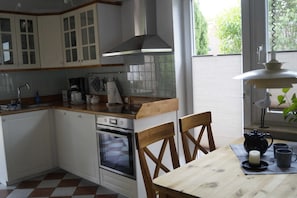 Eine Küche mit weißen Schränken, einer Holz Arbeitsplatte, einem Backofen, einem Spülbecken und einem Fenster mit Blick auf Grünflächen.