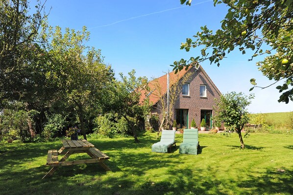 A house with a brick exterior, a green door, and a garden with a picnic table and two lounge chairs.