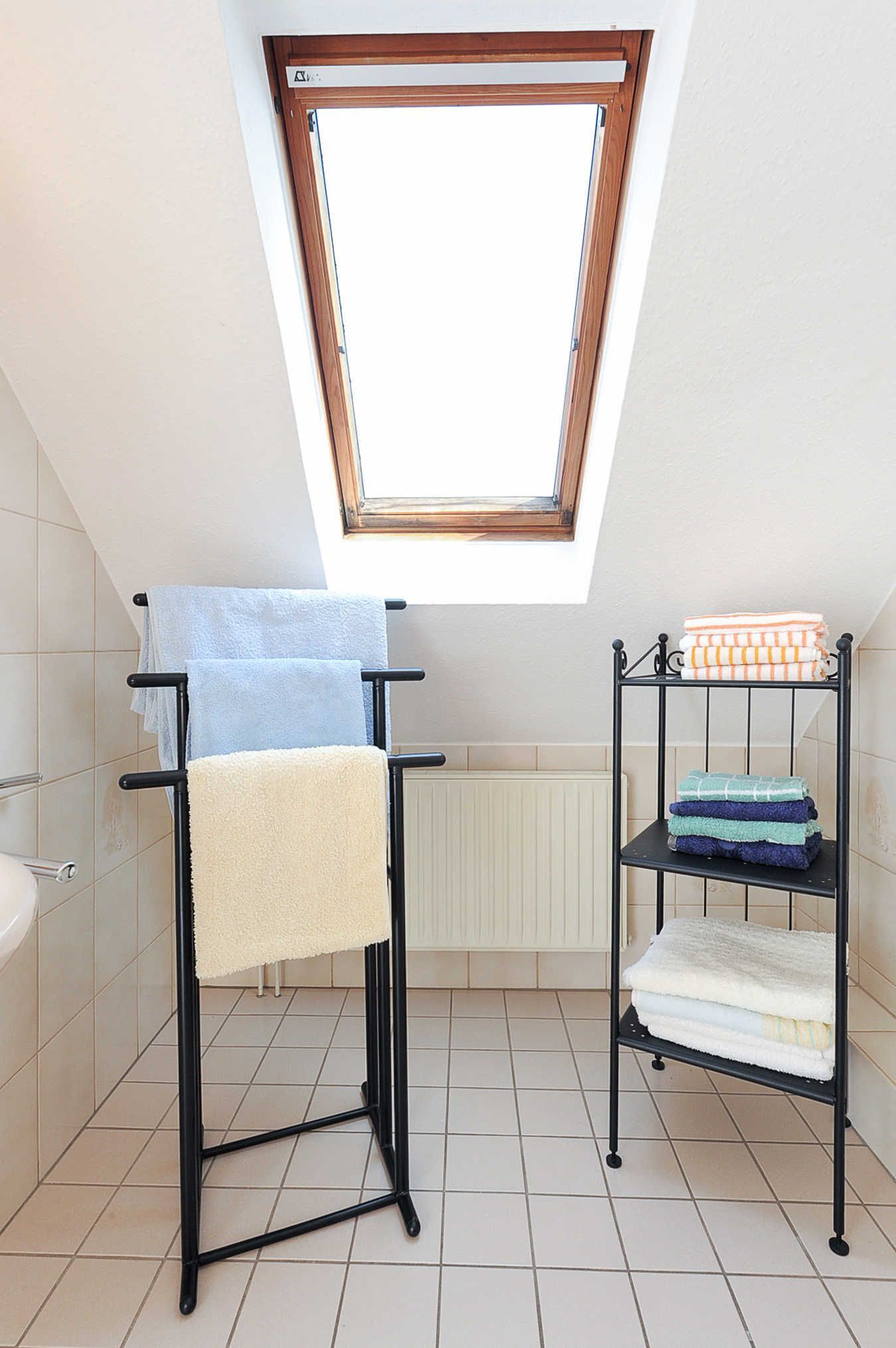 A bathroom with a skylight, a towel rack, and a shelf with folded towels.