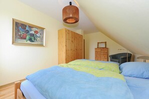A bedroom with a bed, a wooden wardrobe, a chair, a dresser, and a painting on the wall.