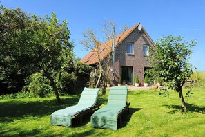 A house with a brick exterior, a red roof, and a green door. There are two lounge chairs in the front yard.