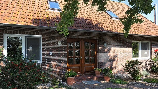 A two-story house with a brick facade, a wooden front door, and a tiled roof. - Ferienwohnung Verklicker - Ferienwohnungen im Haus am Watt in Ostbense (Neuharlingersiel)