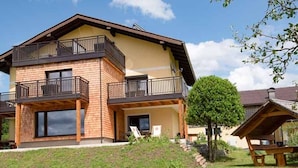 A two-story house with a balcony, a small garden, and a picnic table.