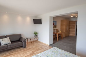 A modern living room with a sofa, a small table with a plant, a TV mounted on the wall, and a dining area visible through an open doorway. - Tilda - Schöbringer Farm (Miglberg)