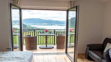 Une chambre avec un lit, un canapé, un balcon avec des fauteuils en osier et une table décorée de fleurs.