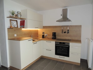 A modern kitchen with white cabinetry, a stainless steel range hood, a built-in oven, and a wooden countertop. - Tilda - Schöbringer Farm (Miglberg)