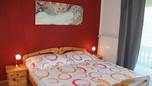 Une chambre à coucher avec un lit en bois, deux tables de chevet, une lampe de chevet, un tableau au mur et une fenêtre avec des rideaux.