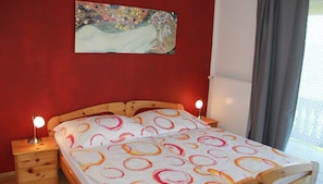 A bedroom with a wooden bed, two bedside tables, a night lamp, a painting on the wall, and a window with curtains. - Tilda - Schöbringer Farm (Miglberg)