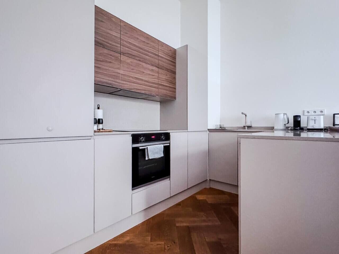 A modern kitchen with white cabinetry, a built-in oven, and a wooden accent wall.