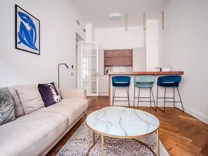 A modern living room with a sofa, a marble coffee table, and a kitchen area with bar stools.