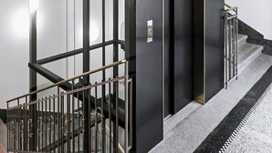 Un ascensor moderno con detalles metálicos, paneles de vidrio y un botón de emergencia visible.