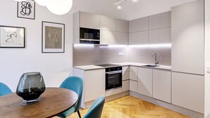 Una cocina moderna con armarios blancos, un horno negro y un microondas de acero inoxidable. Hay una mesa de comedor con sillas y una copa de vino encima.