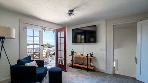 Ein Wohnzimmer mit einer Couch, einem Hocker und einem an der Wand befestigten Fernseher.