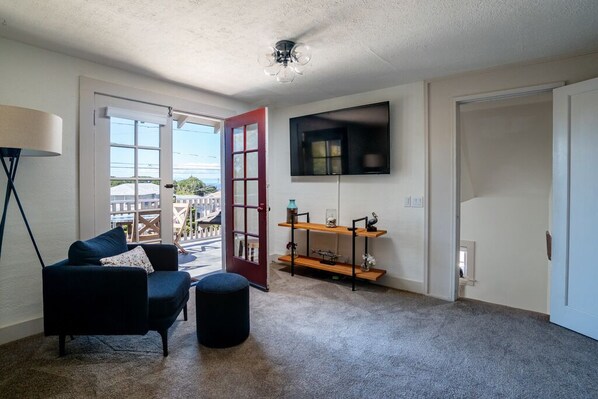 A living room with a sofa, ottoman, and a TV mounted on the wall. - Latitude Adjustment - Pacific Grove Duplex - Ocean View, Walk to Town, Pet Friendly! (Pacific Grove)