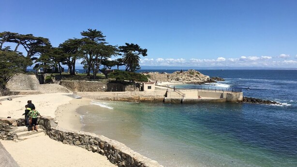 Ein Strand mit einer Steinmauer, einem kleinen Gebäude und Bäumen.