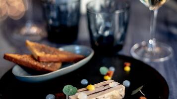 Un plato de postre con una porción de pastel, adornos y dos copas de vino sobre una mesa.
