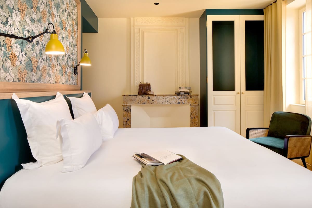 A hotel room with a bed, a desk, a chair, and a wall with a floral pattern.