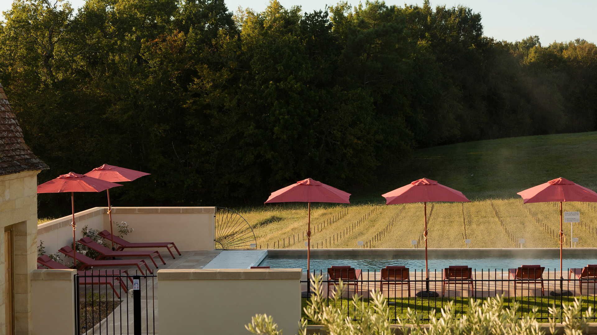 A poolside area with red umbrellas, lounge chairs, and a view of a forested area.