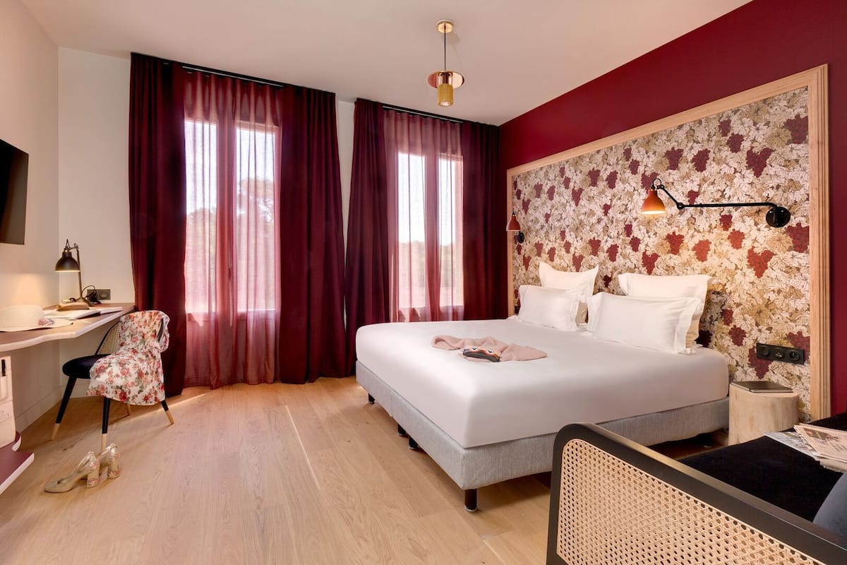 A hotel room with a bed, desk, chair, and a large floral-patterned headboard.