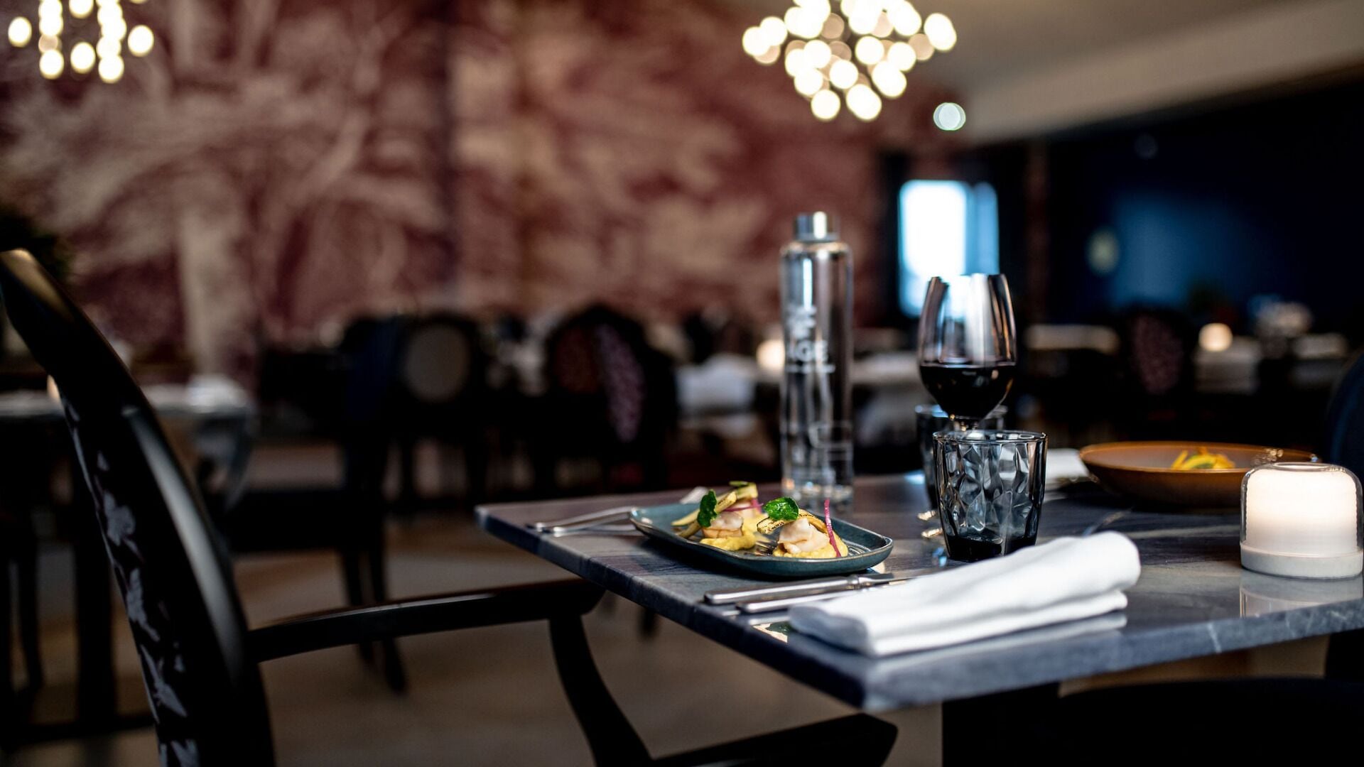 A dining table with a plate of food, a wine glass, and a candle.