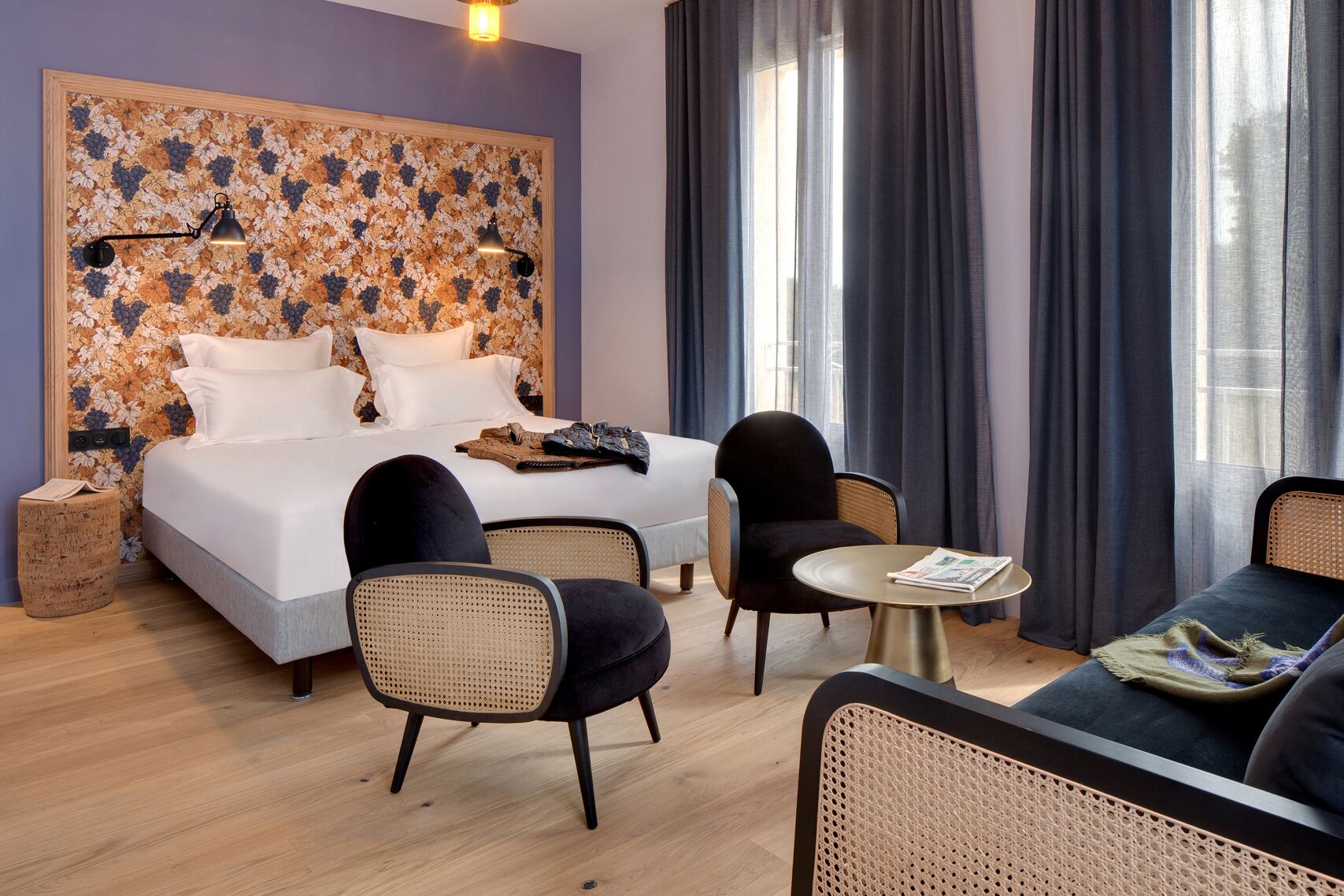 A hotel room with a bed, two chairs, a small table, and a large window with curtains.