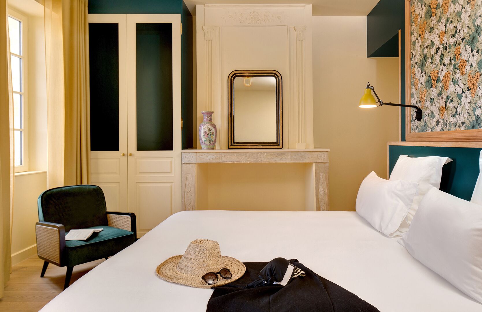 Habitación de hotel con cama, silla, espejo, florero y lámpara.