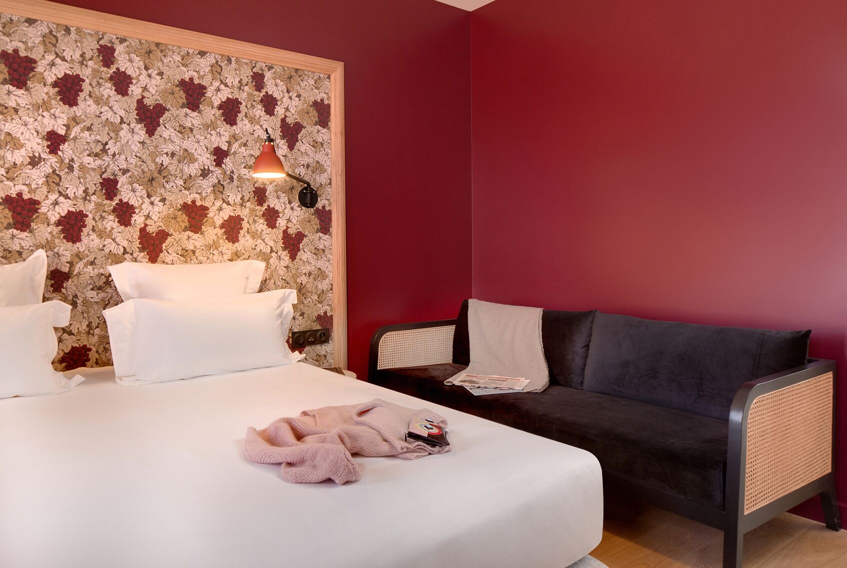 A hotel room with a bed, a dark sofa, and a wall with a floral pattern.